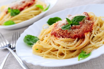 piatto bianco con spaghetti al sugo e parmigiano grattugiato e basilico fresco