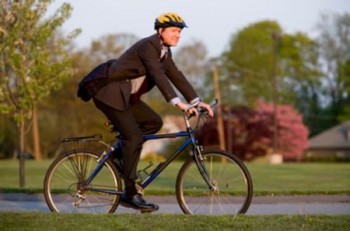 uomo vestito elegante con giacca e cravatta che va in bicicletta con caschetto giallo in testa